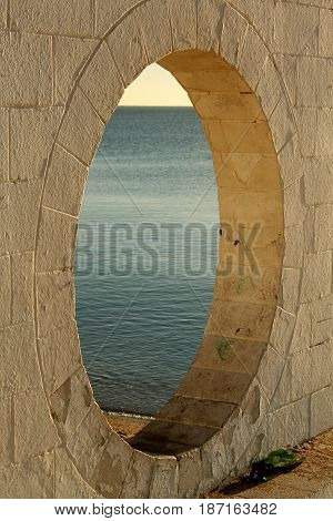 Round architectural window with the sea behind.