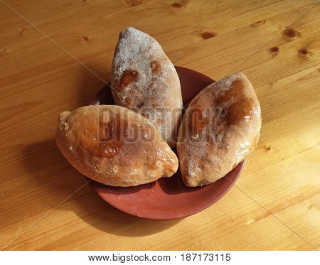 Three small pies in the brown plate. Russian homemade pirozhki at wooden table.