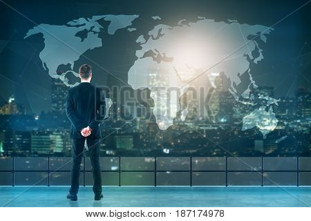 Back view of young businessman on rooftop looking at abstract map. Night city background. Travel concept
