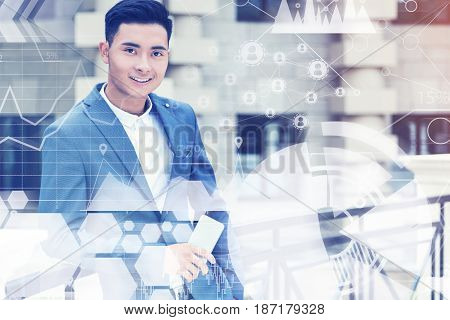 Portrait of a young handsome Asian businessman in a suit standing in a street and holding his smartphone. Graphs in the foreground. Toned image