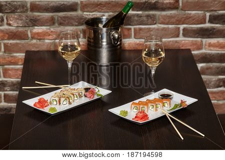 Two sets of sushi rolls on white plate with chopsticks and wine glasses