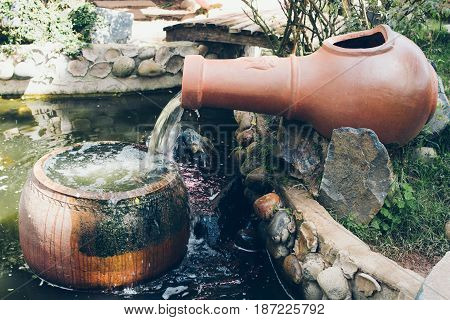 Waterfall made with ceramic jar. Decorative garden red pots in little pond