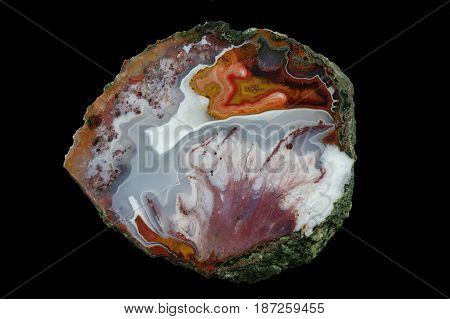 A cross section of the agate stone. At the top is concentic agate at the bottom is a colored pseudomorphosis after dissolved minerals. Multicolored silica rings colored with metal oxides are visible. Origin: Asni Atlas Mountains Morocco.