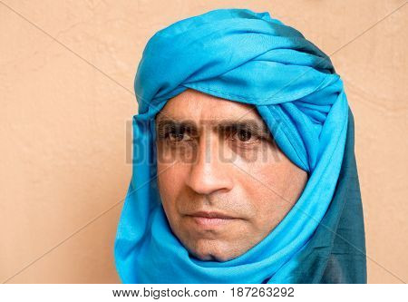 Portrait of a middle aged man standing in front of a mud wall in Morocco Africa wearing a blue Moroccan shesh a Touareg turban.