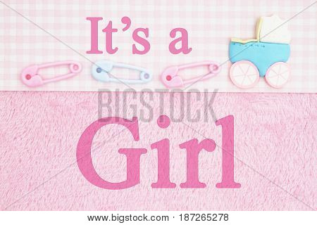 Old fashion It's a girl message Baby diaper pins and a baby carriage with pink fabric background and text It's a Girl