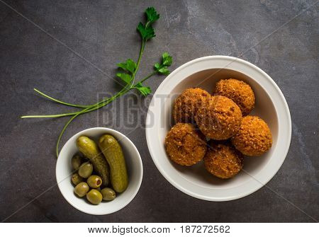 A popular arabic snack - Falafel. A bowl full of fried Falfel with pickle and strands of green parsely.