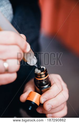 Close-up man is filling an electronic cigarette with a fragrant liquid on a fleece. The spiral is hot. The concept of replacement of cigarettes with tobacco, harmless smoking.