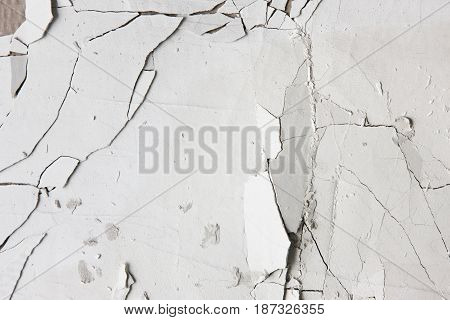 Cracked old white stucco wall, closeup. Pieces of peel plaster. Repair background with free space. Error in the technology of application of building materials