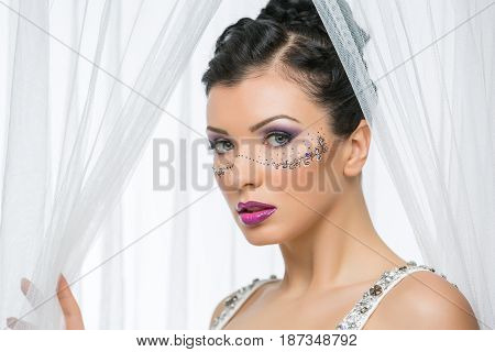 Beautiful young woman in wedding gown with make-up and mask drawn around eyes. Bride with big white bow on head.  Beauty closeup shot.