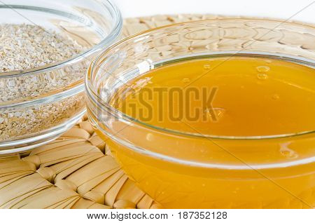Oat bran and honey in a glass bowl on straw hot pad. Closeup shot. Healthy food concept.
