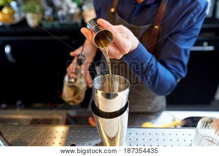 drinks, people and luxury concept - bartender pouring alcohol from jigger into shaker and preparing cocktail at bar