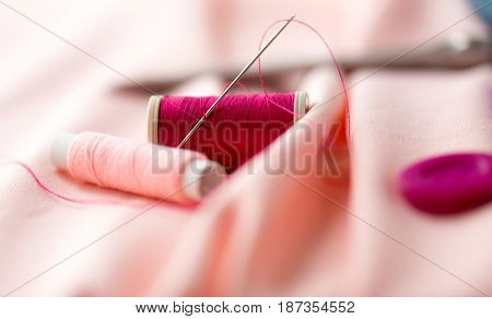 needlework and tailoring concept - sewing needle, spools of thread and cloth
