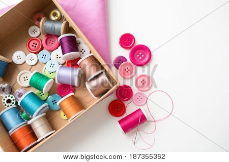 needlework, craft, sewing and tailoring concept - box with thread spools and buttons on table