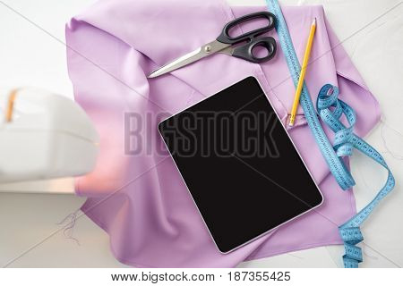 needlework, technology and tailoring concept - sewing machine with tablet pc computer, scissors, tape measure and fabric