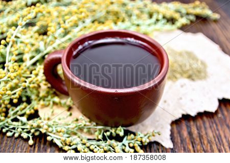 Herbal tea in a brown clay cup, twigs gray sagebrush, wormwood dried on a paper on the background of wooden boards