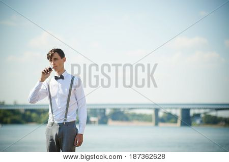 Young Skinny Man, Elegantly Stylishly Dressed In White Shirt, Trousers With Suspenders And Bow Tie.