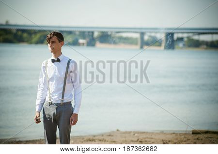 Young Skinny Man, Elegantly Stylishly Dressed In White Shirt, Trousers With Suspenders And Bow Tie.