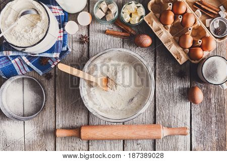 Baking background. Cooking ingredients for dough and bowl with flour on rustic wood.