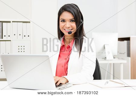 Businesswoman wearing microphone headset using laptop computer in the office - operator call center telemarketing and customer service staff concepts