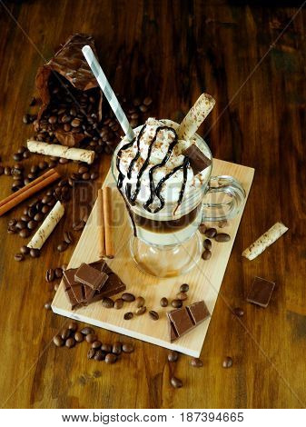 Coffee cocktail with whipped cream in an Irish coffee mug surrounded by coffee beans, cinnamon and chocolate bars