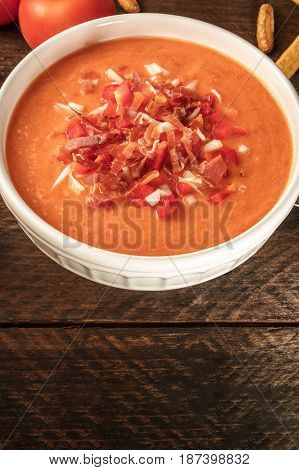 Photo of gazpacho, traditional Spanish soup, garnished with jamon, tomato and onion slices, on a dark rustic background with place for text