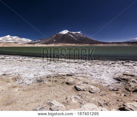 laguna verde and salty surface with snow-covered peak on background in atacama desert in chile with vlue sky