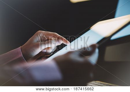 Girl using a tablet with a clean blank screen display in an business office atmosphere on the keyboard and cup of coffee on the wooden table background digital gadget in female hands in the night workspace atmosphere