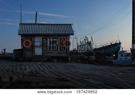 SOLOVKI ISLANDS, RUSSIA, AUG, 10, 2015: View on old wooden pier with shed house with red flotation rings and very old ship fish trawler on the back. Tourists famous sightseeing places in Russia