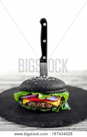 Close up of Homemade Black Burger with Cheese. Cheeseburger with black bun on white wooden background. Junk food.