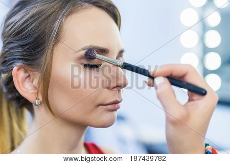 Make-up artist doing smoky eyes makeup to beautiful young girl in the studio Dressing room