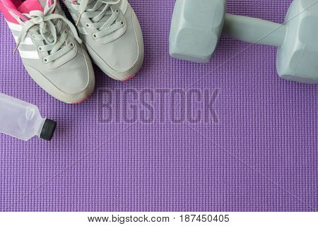 Fitness background with sport shoes gray dumbbells and water over violet yoga mat in gym Healty and lifestyle concept