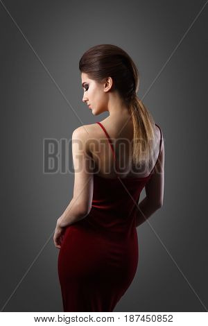 Beautiful woman with evening make-up and updo. Fashion photo. Girl wearing red dress ower dark background. Studio shoot.