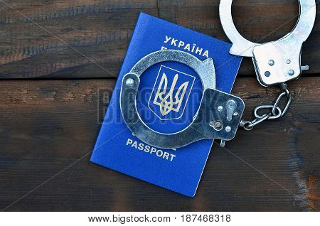 Ukrainian Passport With Police Handcuffs Lies On A Wooden Table. The Concept Of Crime Of Ukrainian C
