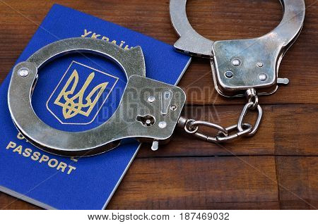 Ukrainian Passport With Police Handcuffs Lies On A Wooden Table. The Concept Of Crime Of Ukrainian C