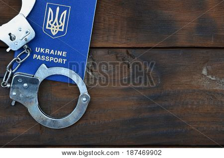 Ukrainian Passport With Police Handcuffs Lies On A Wooden Table. The Concept Of Crime Of Ukrainian C