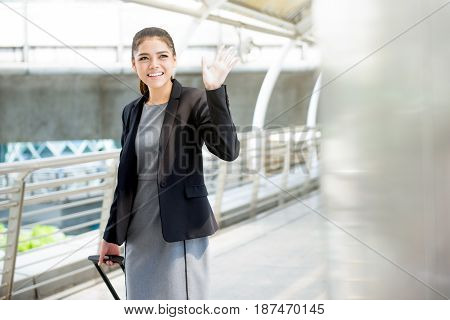 Young Asian businesswoman with baggage waving hand bye bye - business travel concept