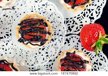 Strawberry cake with vanilla cream on white rusric wooden background. Sweet basket tartlet with strawberries and chocolate. Tasty summer dessert. Top view.
