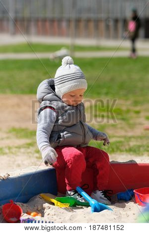 Portrait of toddler child wearing vest jacket outdoors. One year old baby boy playing with sand at playground sandbox