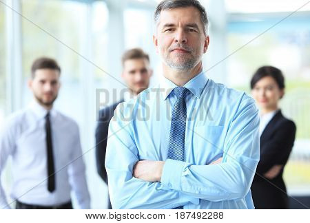 Mature smiling business manager crossing his arms in front of his business team