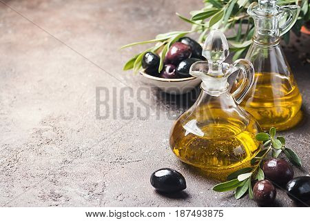 Olive oil in a glass bottle and olive branch on brown stone table