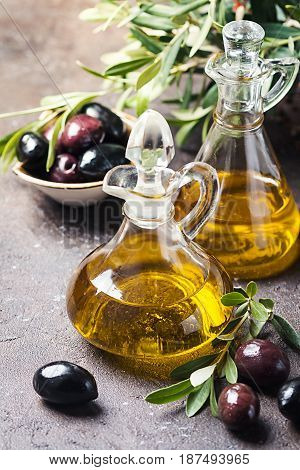 Olive oil in a glass bottle and olive branch on brown stone table