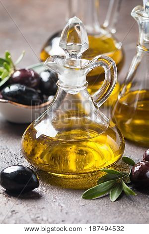 Olive oil in a glass bottle and olive branch on brown stone table