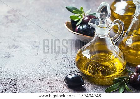 Olive oil in a glass bottle and olive branch on brown stone table