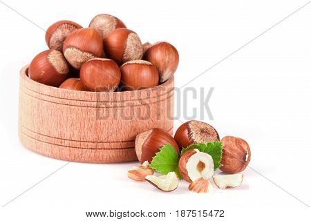 Hazelnuts with leaves in a wooden bowl isolated on white background.