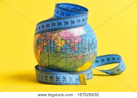 Measuring tape wrapped around terrestrial globe isolated on yellow background. Symbol of worldwide economy population and migration issues