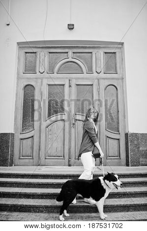 Trendy Girl At Glasses And Ripped Jeans With Russo-european Laika (husky) Dog On A Leash, Against Wo