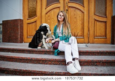 Trendy Girl At Glasses And Ripped Jeans With Russo-european Laika (husky) Dog On A Leash, Against Wo