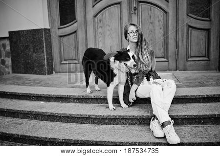 Trendy Girl At Glasses And Ripped Jeans With Russo-european Laika (husky) Dog On A Leash, Against Wo