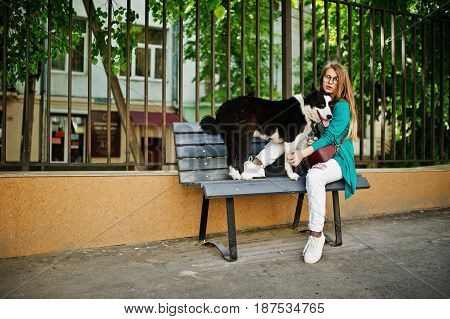 Trendy Girl At Glasses And Ripped Jeans With Russo-european Laika (husky) Dog On A Leash, Against Be