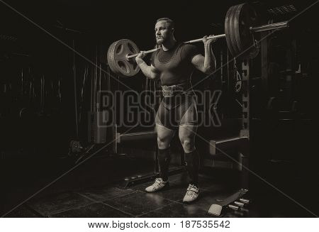 Professional athlete makes squats with a bar in the gym
